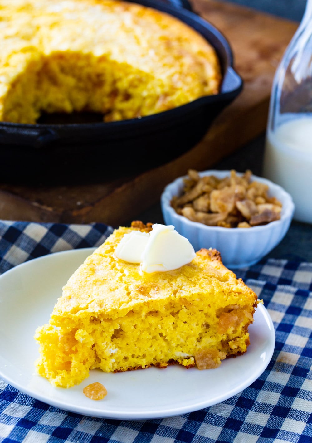 Slice of cornbread on a plate with casto iron pan full of cornbread in background.