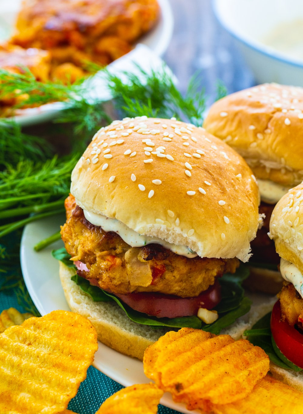 Three Crawfish Burgers on a plate with chips.