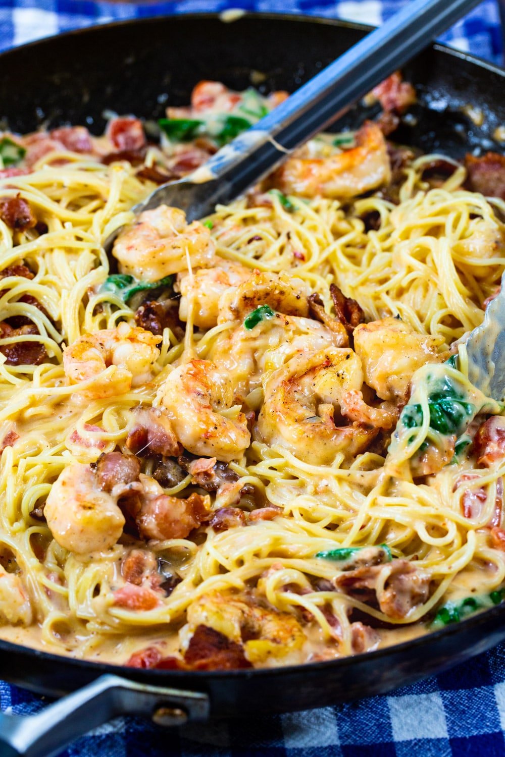 Tongs scooping up Creamy Angel Hair Pasta with Bacon and Shrimp.