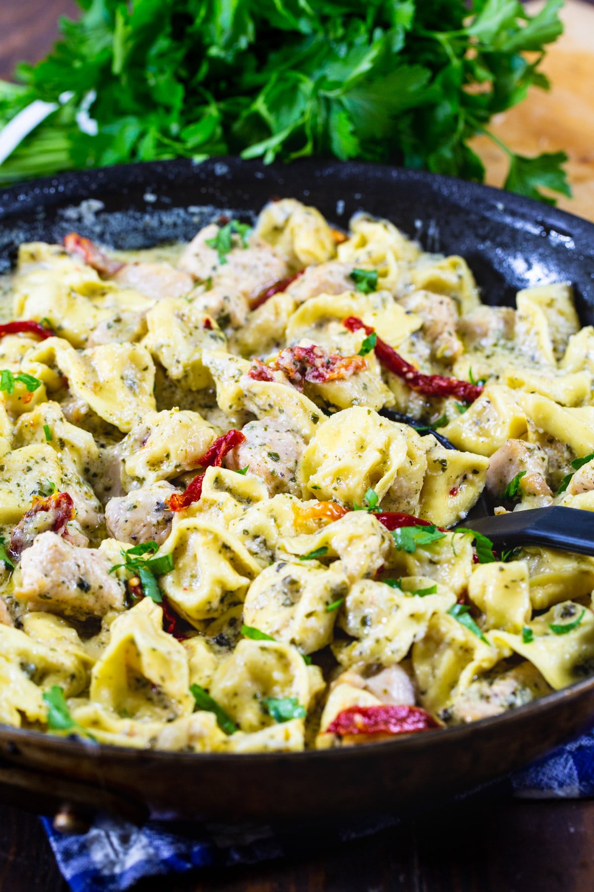Pesto Tortellini in a skillet with parsley behind it.
