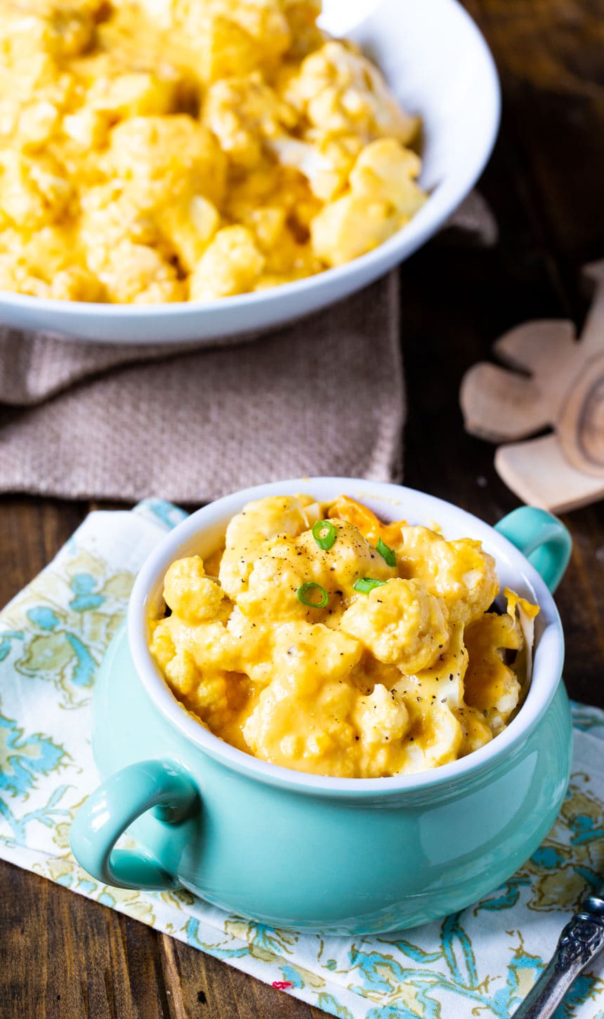 Bowl of Cauliflower and Cheese with large serving bowl in background.