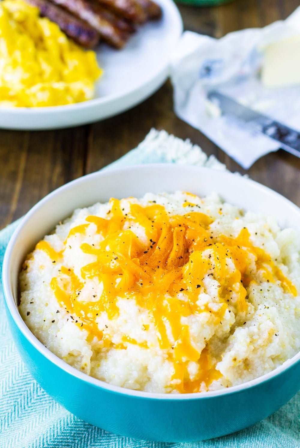 Bowl full of grits with bacon and eggs in background.