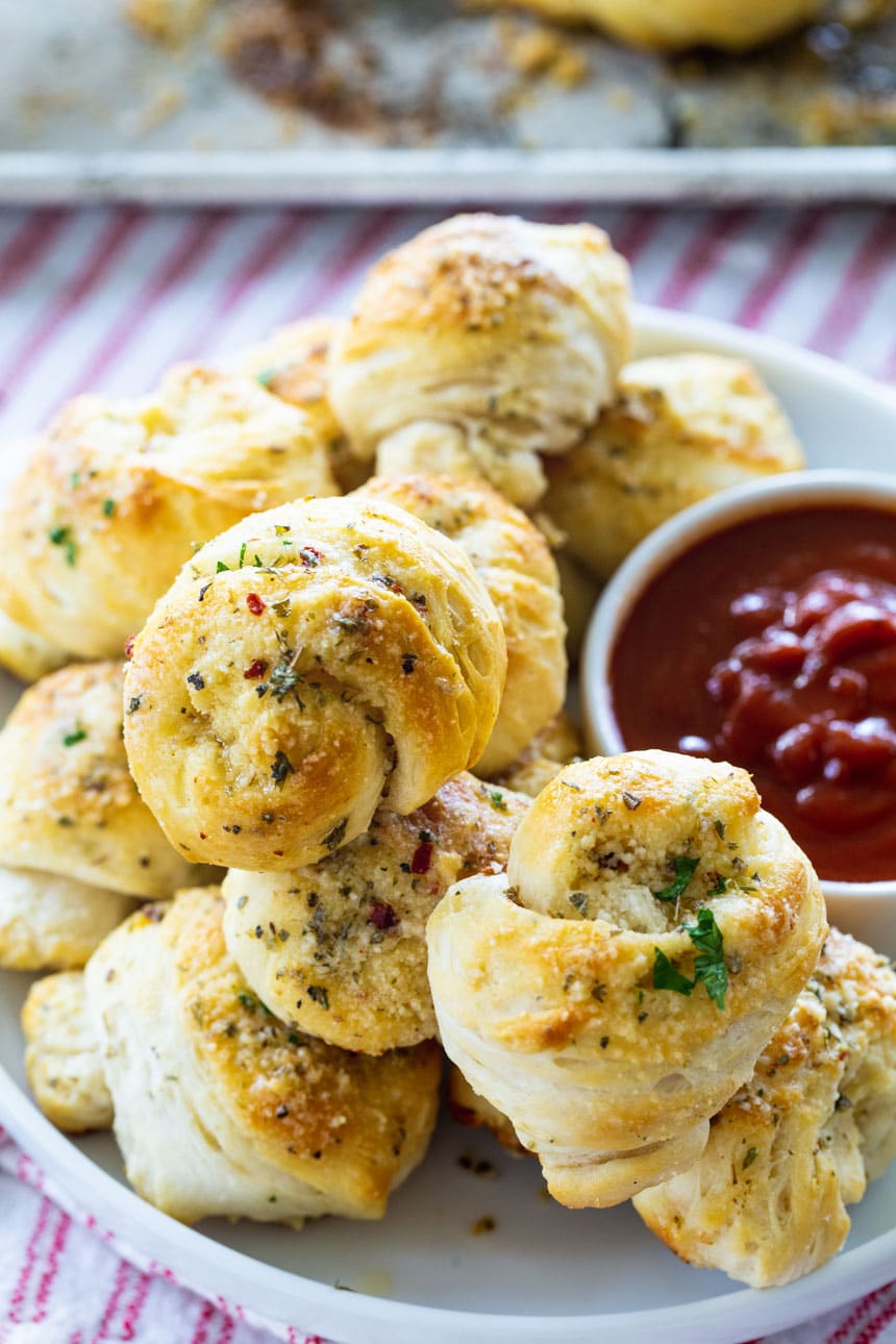 Garlic Knots stacked on a plate with pizza sauce.
