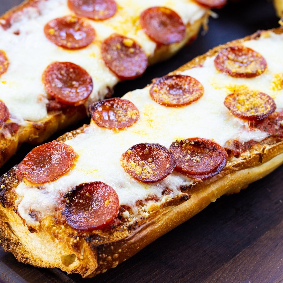 Two Pieces of Pepperoni French Bread Pizza on a cutting board.