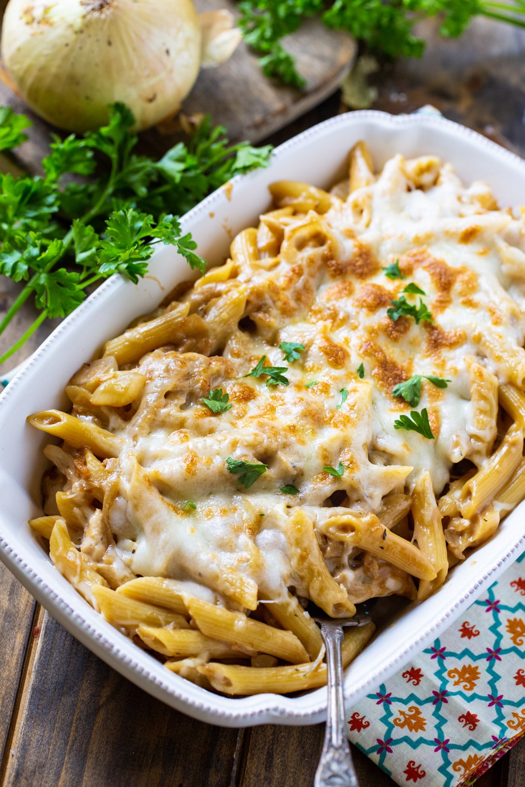 Pasta with melted cheese in a casserole dish and a bunch of fresh parsley.