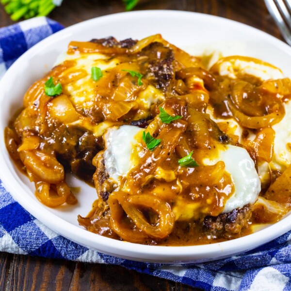 French Onion Salisbury Steak over mashed potatoes on a white plate.