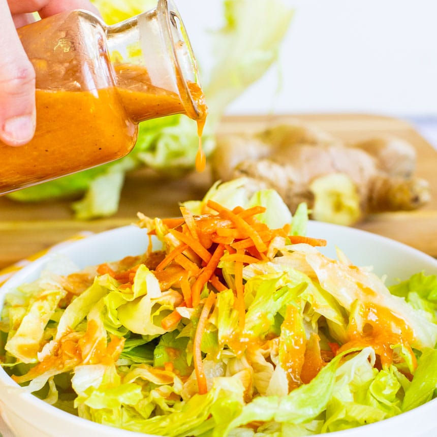 Pouring salad dressing over a green salad with carrots.