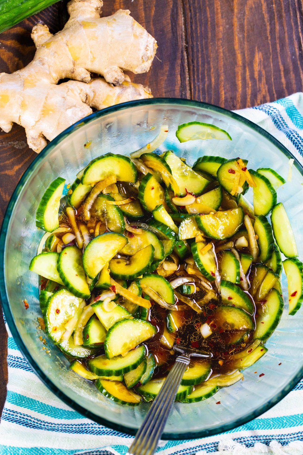 Cucumbers with all the dressing ingredients in a glass bowl.