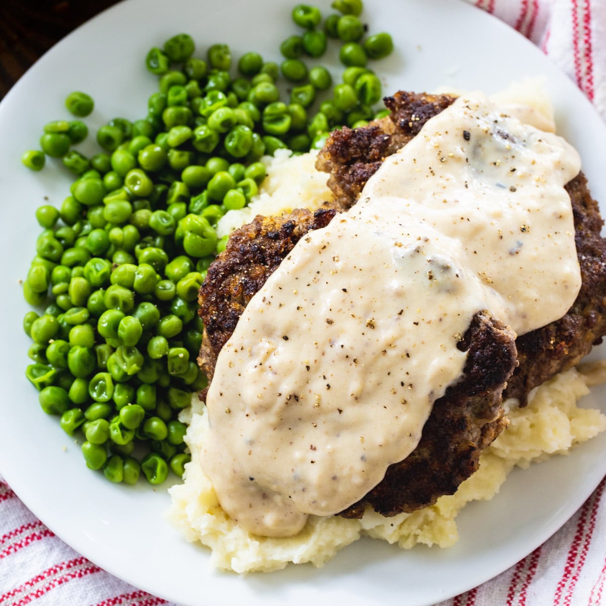 Hamburger Steaks over mashed potatoes with peas.