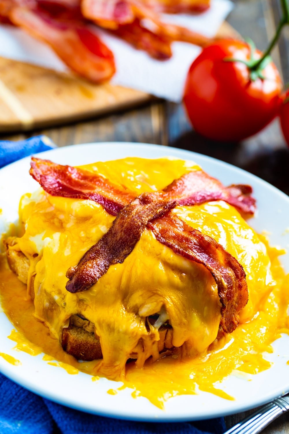 Hot Brown Sandwich on a plate with bacon and tomatoes in background.