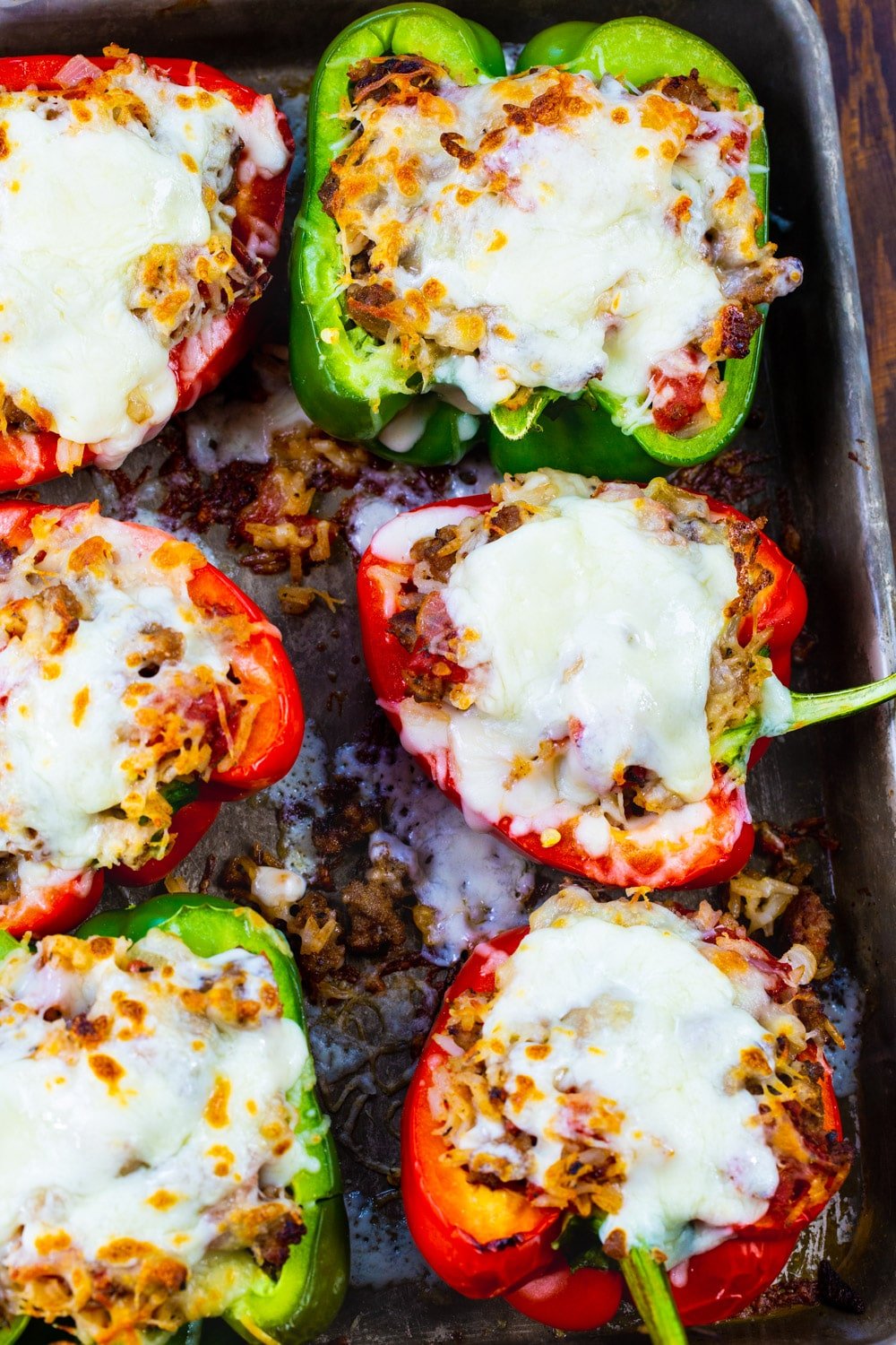 Six cooked stuffed peppers on baking sheet.