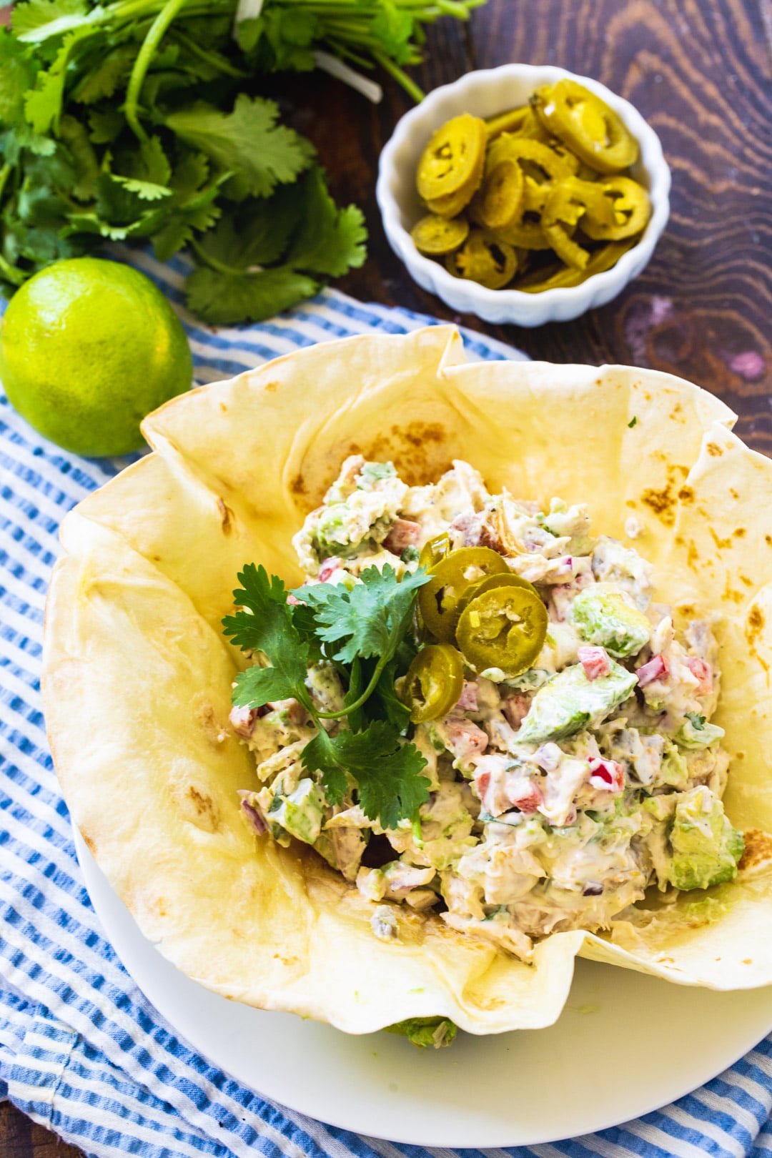 Chicken Salad in a torilla shell surrounded by fresh cilantro and bowl of pickled jalapenos.