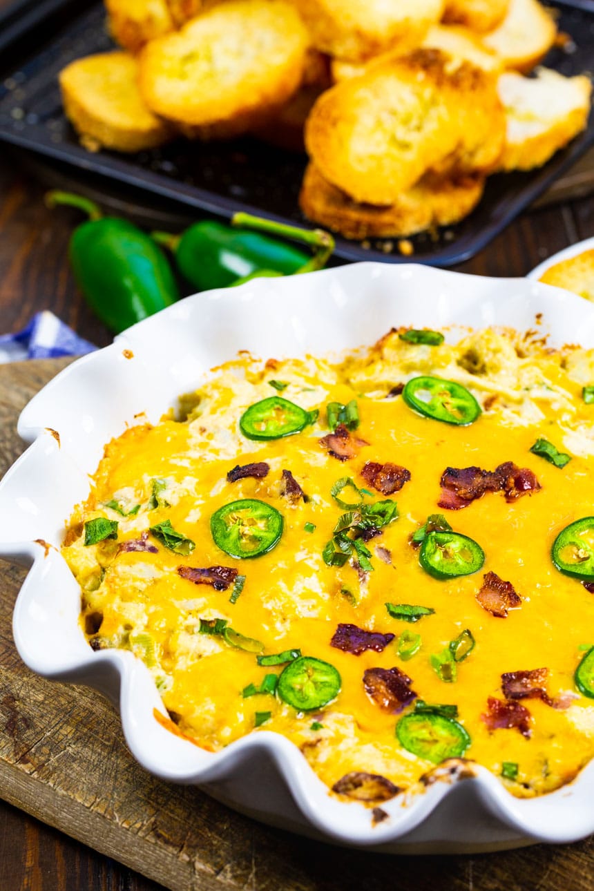 Crab Dip in a white baking dish with sliced baguette behind it.