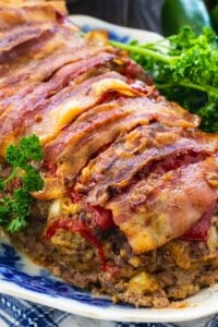 Meatloaf wrapped in bacon on a serving platter with parsley