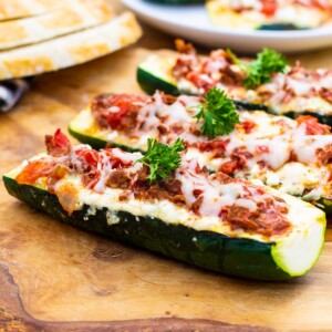 Three Lasagna Zucchini Boats on a wood cutting board.