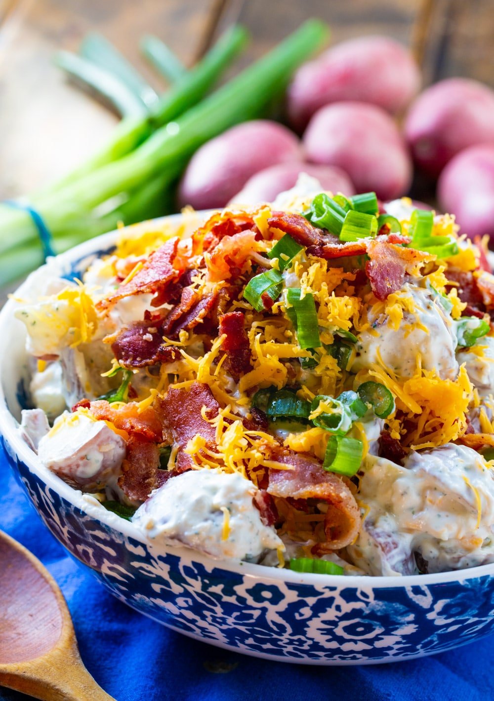 Potato salad in a bowl with potatoes and green onions in background.