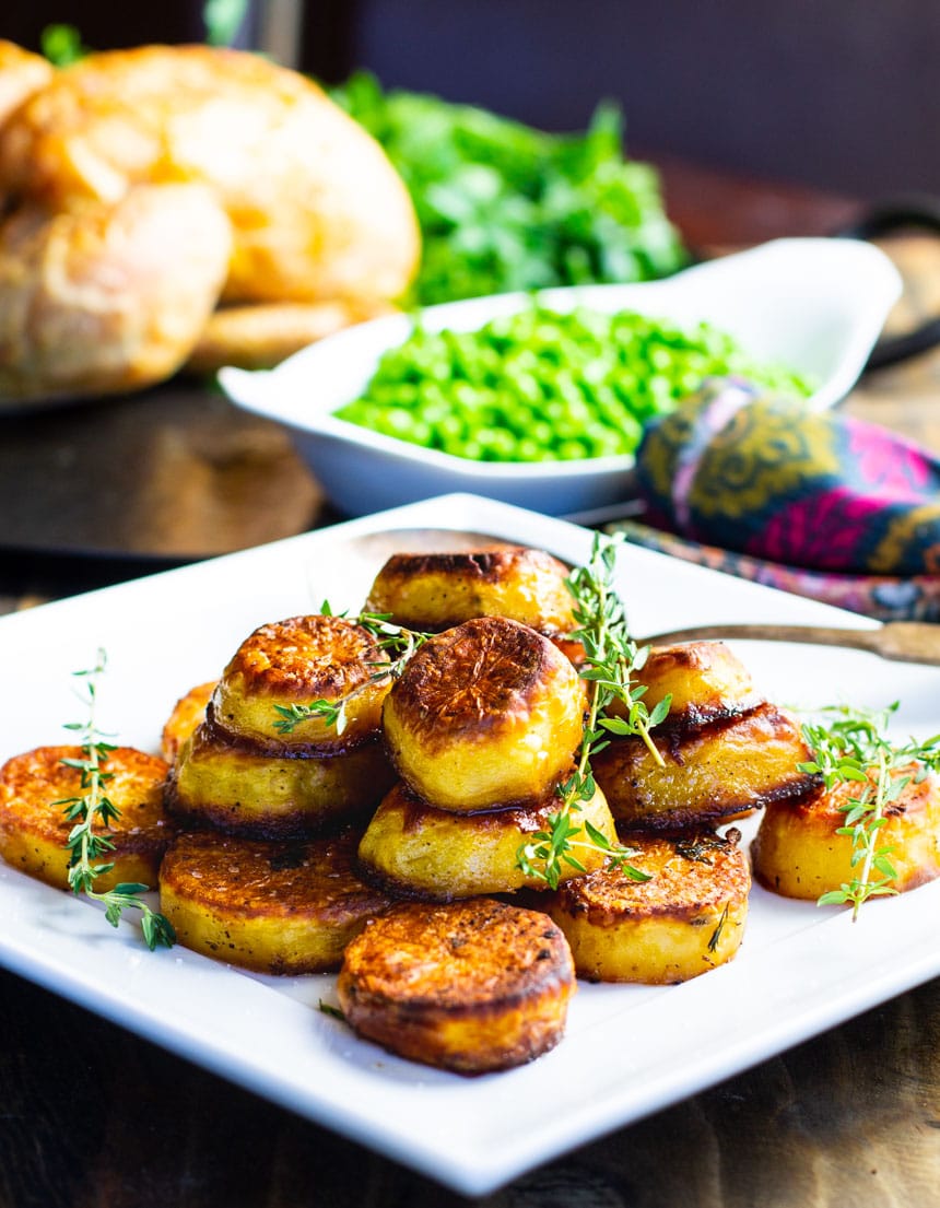 Potatoes on a plate with peas and chicken in background.