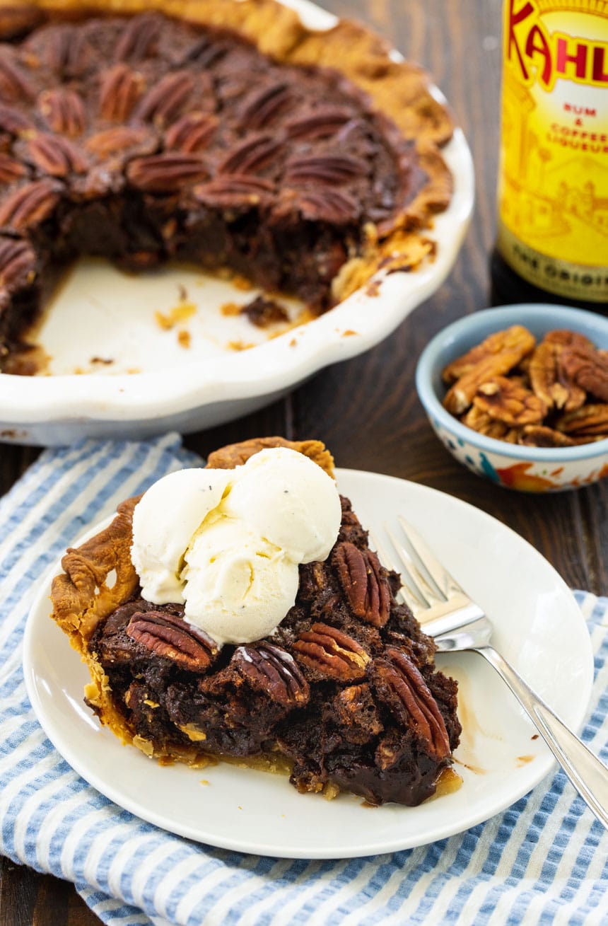 Slice of Pecan Pie on a plate with the rest of the pie in background.