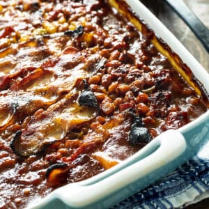 Molasses Baked Beans topped with bacon in a baking dish.