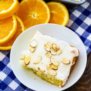 Slice of Orange Almond Sheet Cake on a plate surrounded by orange slices.