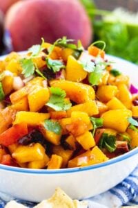 Peach Salsa in a bowl surrounded by fresh peaches and cilantro.