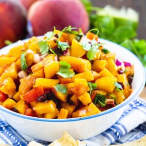 Peach Salsa in a bowl surrounded by fresh peaches and cilantro.