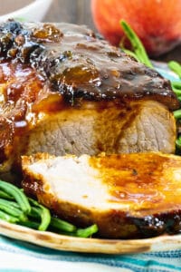 Peach Glazed Pork Roast surrounded by green beans on a serving platter.