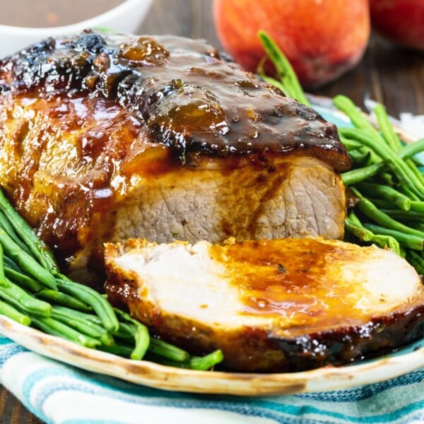 Peach Glazed Pork Roast surrounded by green beans on a serving platter.