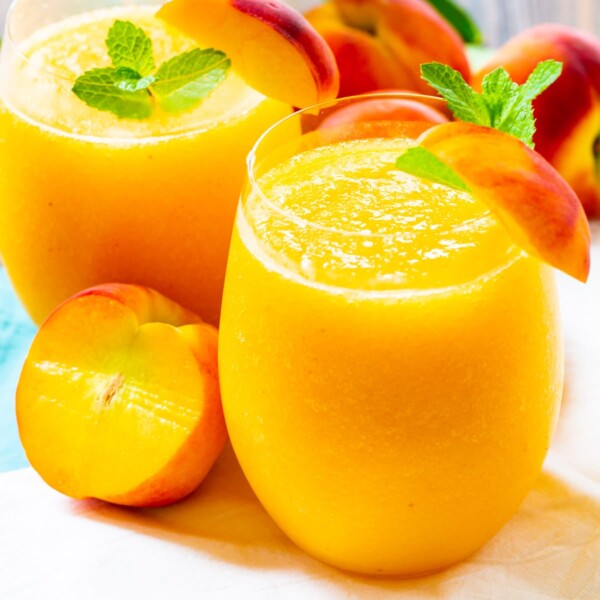 Two Peach Wine Slushies garnished with fresh peaches.