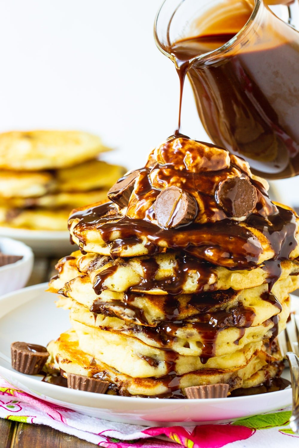 Chocolate sauce being poured on top of stack of pancakes