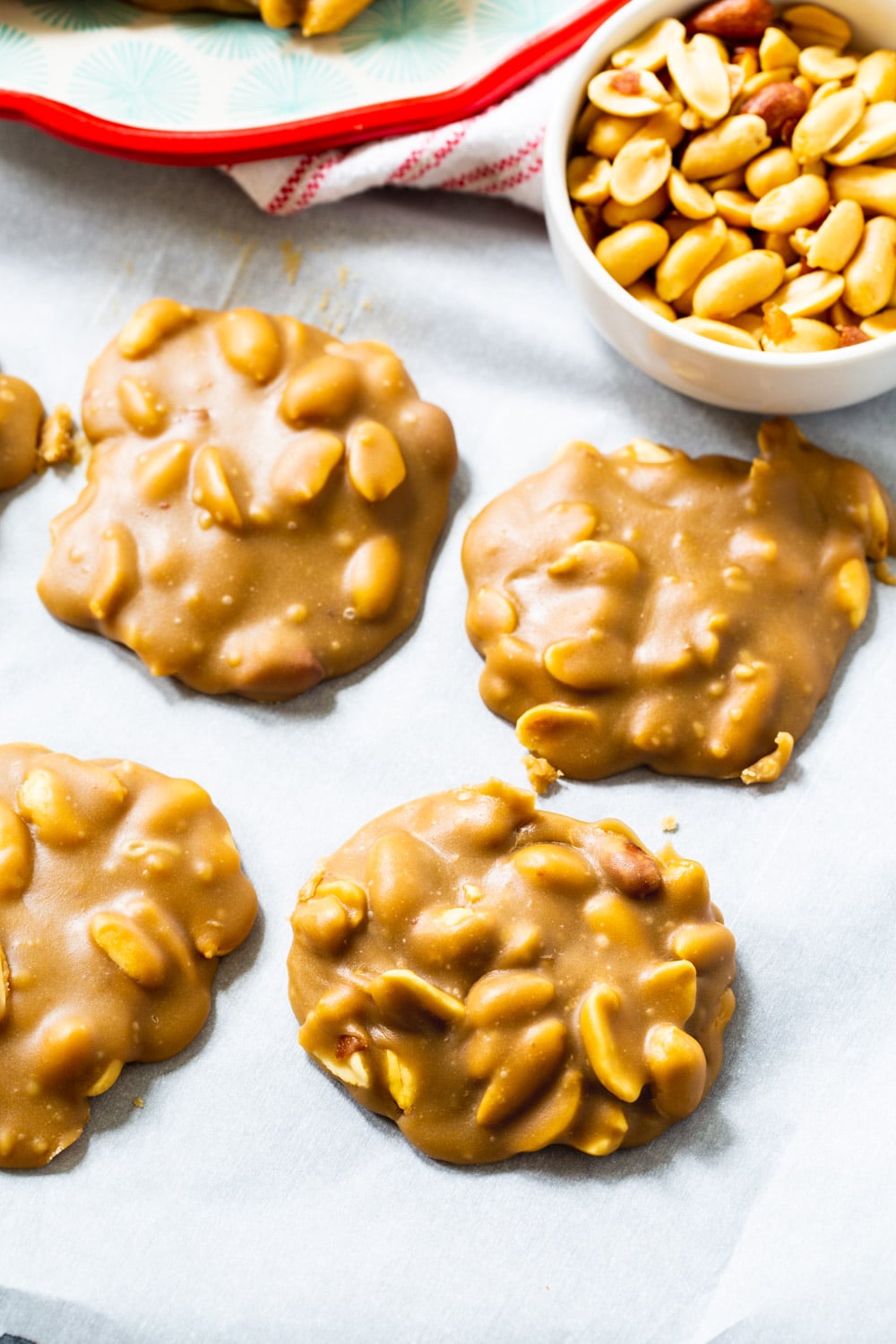 Peanut Pralines on parchment paper with bowl of peanuts.