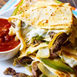 Trinagles of Philly Cheese Steak Quesadilla piled up on plate with bowl of salsa.
