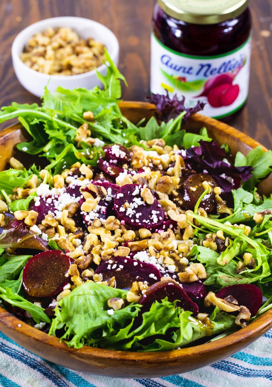 Pickled Beet Salad in wooden bowl with jar of beets and bowl of walnuts.