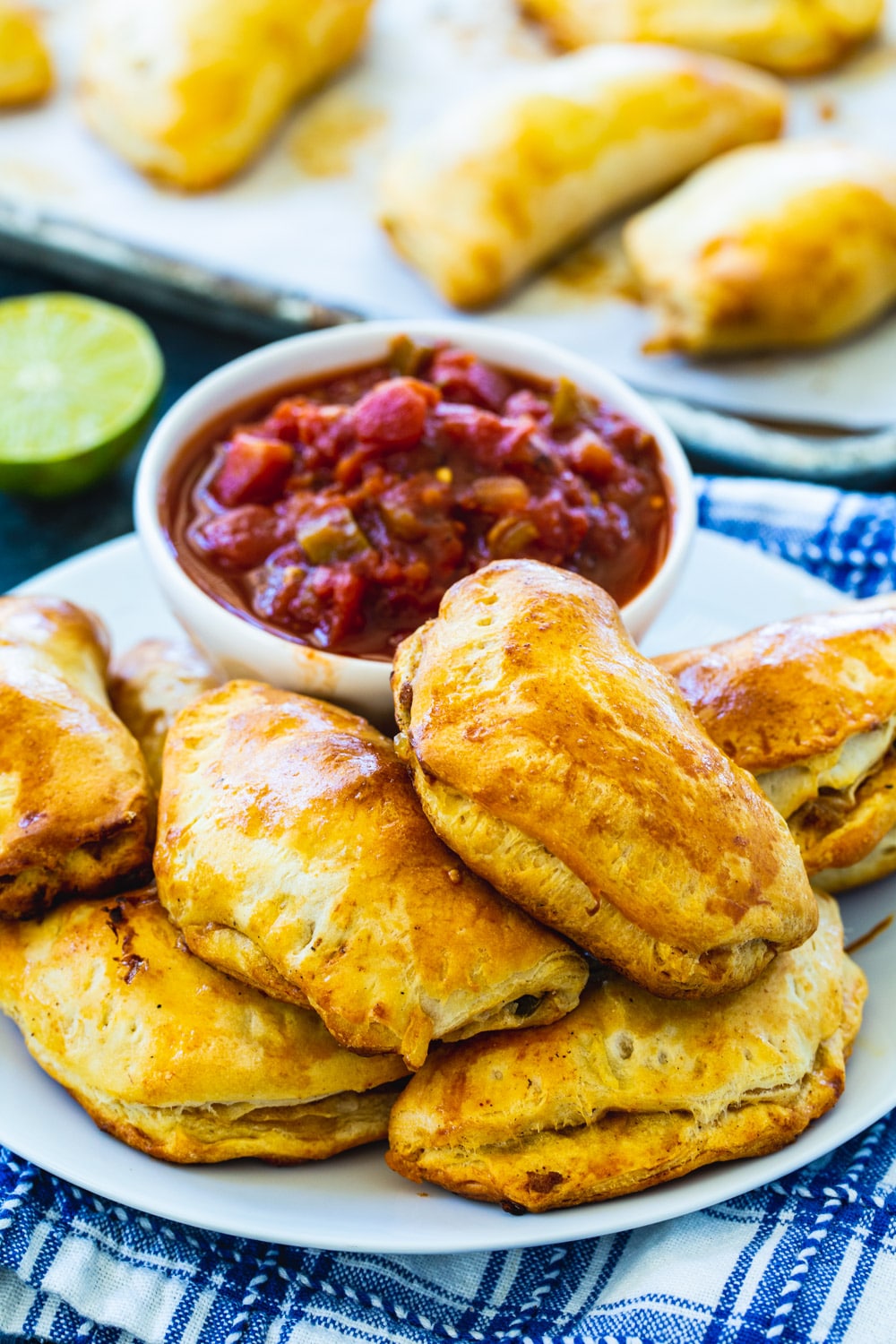Empanadas on plate with salsa with more in background on baking sheet.