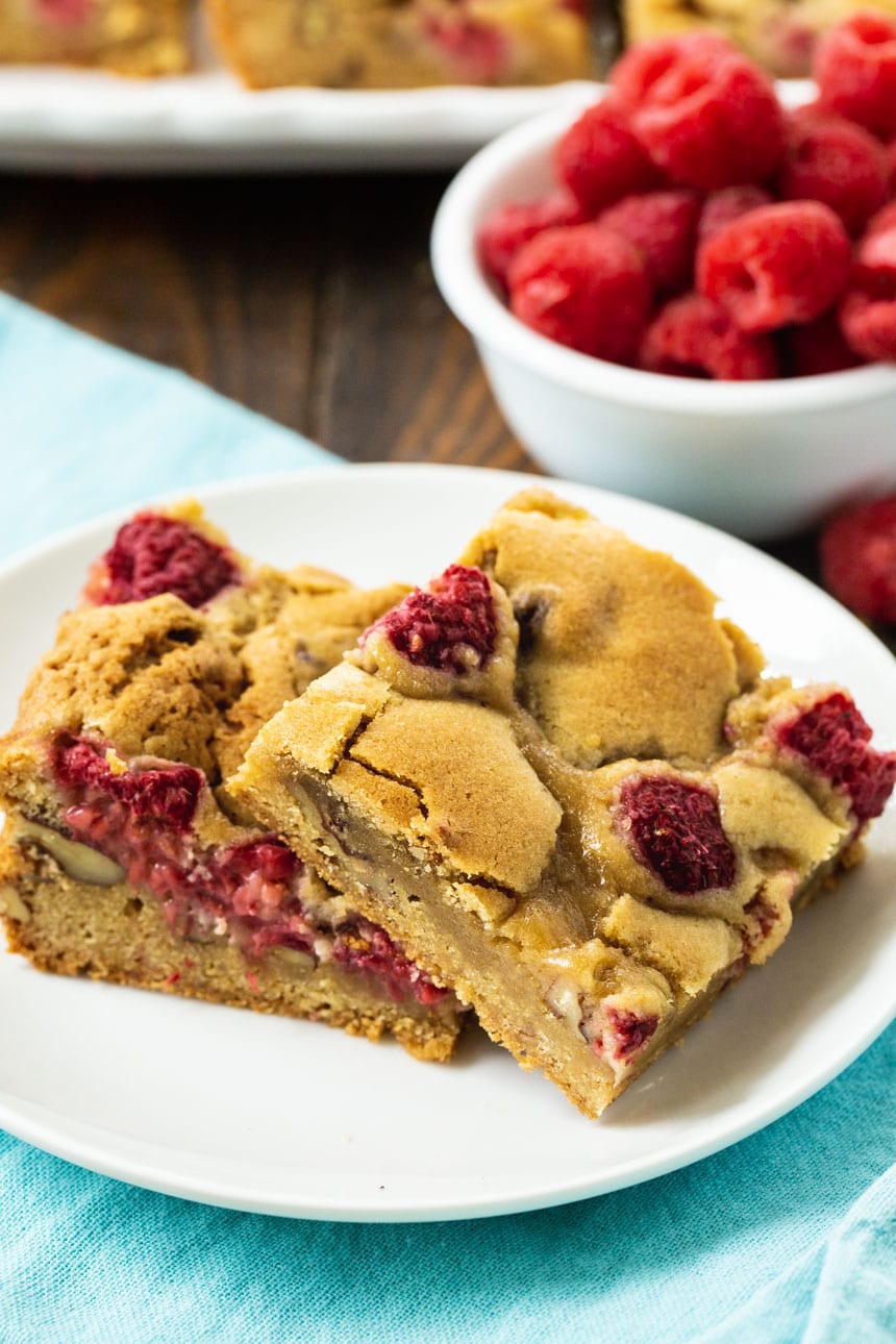 Two Raspberry Pecan Bars on a plate with fresh raspberries in background.