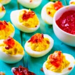 Red Pepper Jelly Deviled Eggs with Bacon on a light blue background.