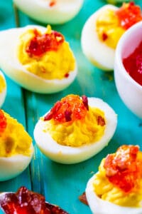 Red Pepper Jelly Deviled Eggs with Bacon on a light blue background.
