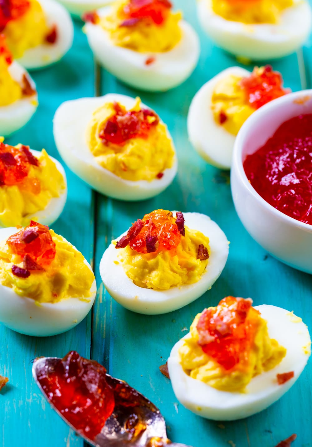 Deviled Eggs topped with Red Pepper Jelly on light blue background.