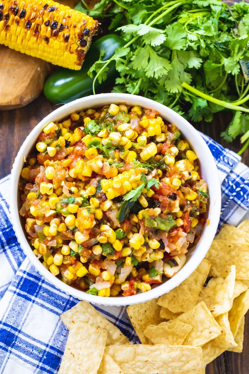 Corn salsa in a bowl with tortilla chips and fresh cilantro surrounding the bowl.