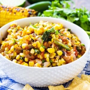 Corn salsa in a white bowl surrounded by tortilla chips and cilantro.