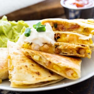 Shrimp, Bacon, and Corn Quesadilla on a plate with guacamole and salsa.