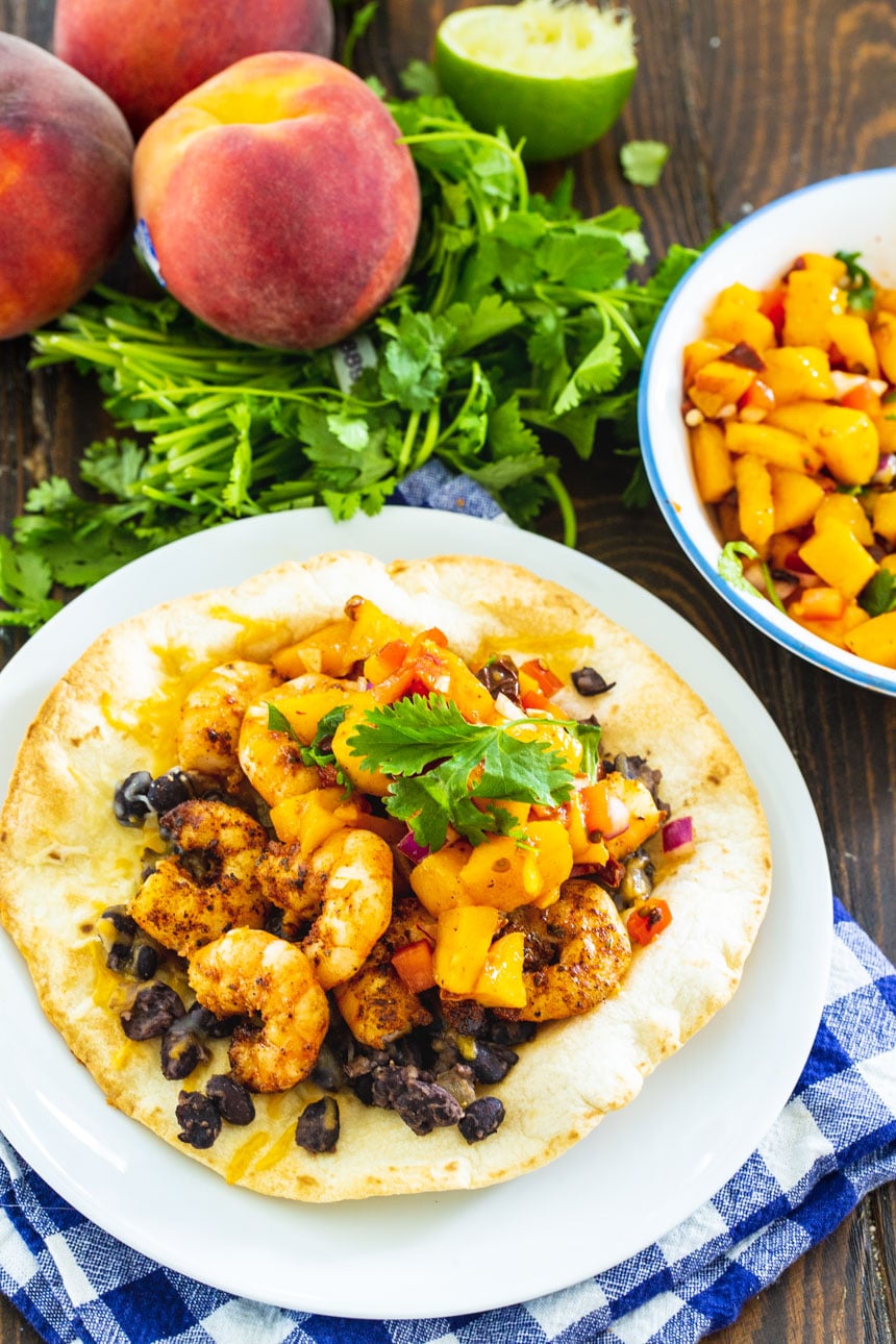 Tostada on a plate with peaches and cilantro in background.