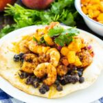 Tostada on a plate topped with black beans, shrimp, and cilantro.