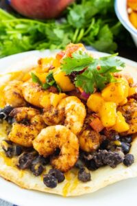 Tostada on a plate topped with black beans, shrimp, and cilantro.