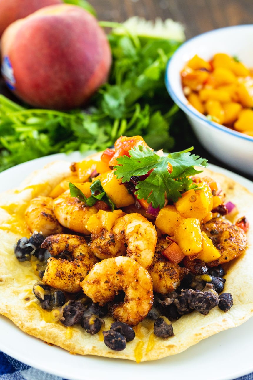 Tostada topped with black beans, shrimp, and peach salsa.