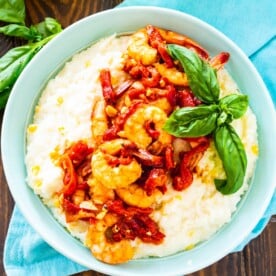 Shrimp and Goat Cheese Grits with Roasted Red Pepper Sauce in a blue bowl with basil.