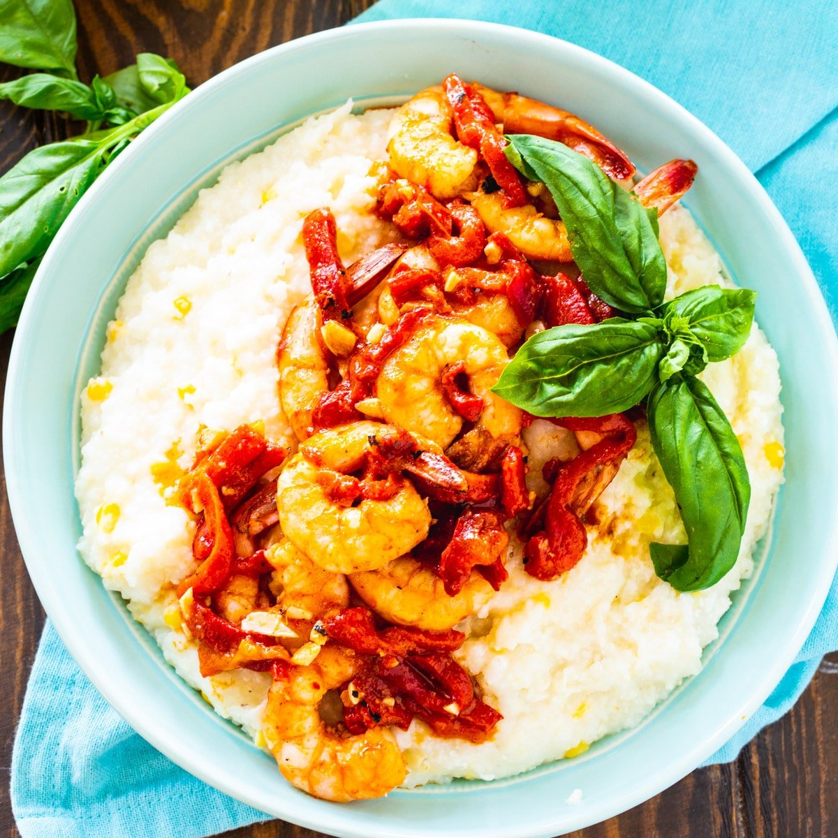 Shrimp and Goat Cheese Grits with Roasted Red Pepper Sauce in a blue bowl with basil.