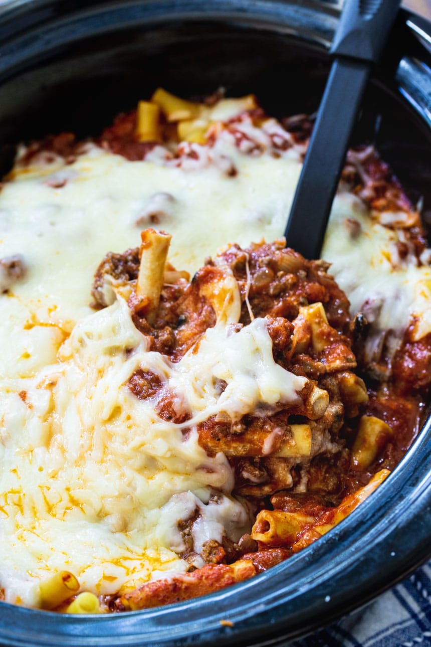 Crock Pot Baked Ziti in a black slow cooker being scooped with a serving spoon.
