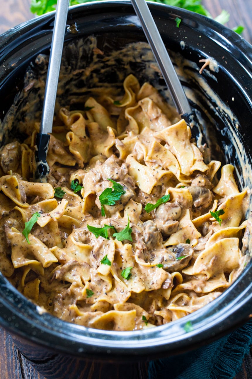 Beef Stroganoff in a slow cooker with tongs.