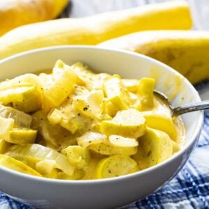 Cheesy Squash in a white bowl with yellow squash in the background.